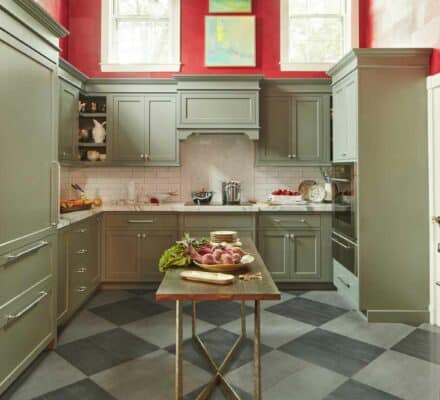A kitchen with green cabinets, a center island with vegetables, checkered floor tiles, red upper walls, and two small windows above—perfect for showcasing a Sub Zero appliance or creating an appliance showroom vibe.