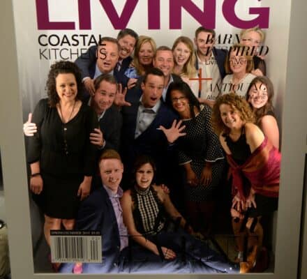 Group of people smiling and posing together for a photo in a stunning kitchen showroom, featured on the cover of New England Living magazine, Fall/Winter 2019 issue.