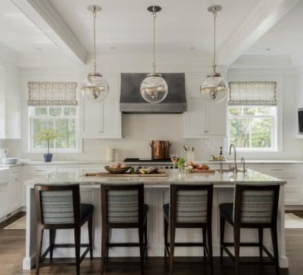 Spacious modern kitchen with white cabinets, stainless steel appliances, a Wolf appliance island with four chairs, pendant lights, and large windows.