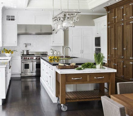 Modern kitchen with white cabinetry, stainless steel appliances—including a Sub Zero appliance—a wooden island on wheels, and fresh vegetables on the countertop, perfect for a kitchen showroom.