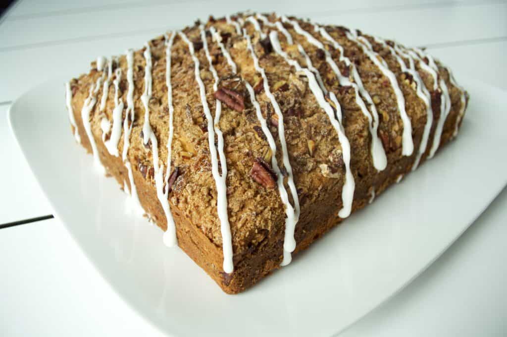 A square coffee cake with crumb topping and pecans, drizzled with white icing, is displayed on a white plate—perfect for enjoying in your kitchen showroom or alongside your favorite luxury kitchen appliance.