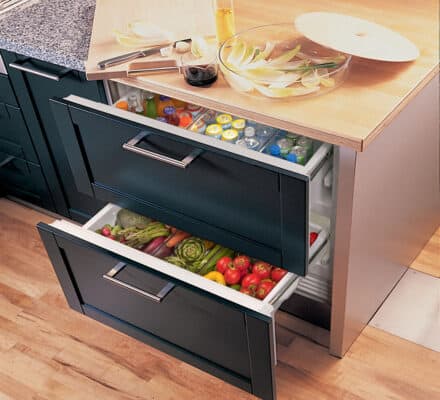 Two open refrigerator drawers built into a kitchen island showcase drinks on top and fresh vegetables and fruits below—a perfect addition for any luxury kitchen appliance display or modern kitchen showroom.