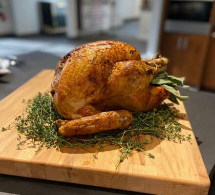 Roast turkey placed on a wooden cutting board, garnished with fresh herbs, in a modern kitchen showroom featuring sleek Wolf appliances.