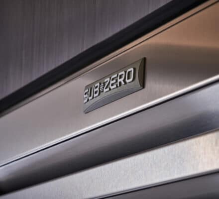 Close-up view of a stainless steel Sub-Zero appliance door in an appliance showroom, showcasing the brand logo on a sleek brushed metal surface.