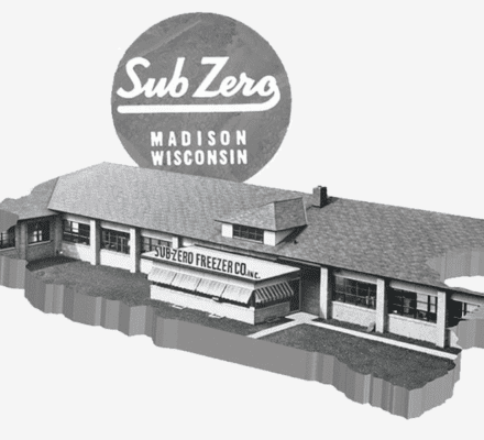 Black-and-white image of the Sub-Zero Freezer Co. building, featuring a large circular sign reading "Sub-Zero Madison Wisconsin" above the roof—a historic icon in luxury kitchen appliance innovation.
