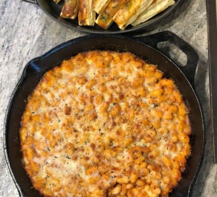 A cast iron skillet filled with baked pasta in tomato sauce, topped with melted cheese, sits on a counter beside a dish of roasted root vegetables—fresh from the oven of a luxury kitchen Wolf appliance.