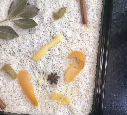 Uncooked white rice in a tray topped with bay leaves, star anise, cinnamon sticks, and citrus peels—an inspiring display you might find in an appliance showroom featuring Wolf and Sub-Zero appliances.