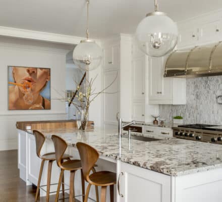 Modern kitchen with white cabinets, a marble island with three wooden chairs, luxury kitchen appliances, stainless steel finishes, and a wall art of a person blowing bubble gum—perfect for a stylish kitchen showroom.