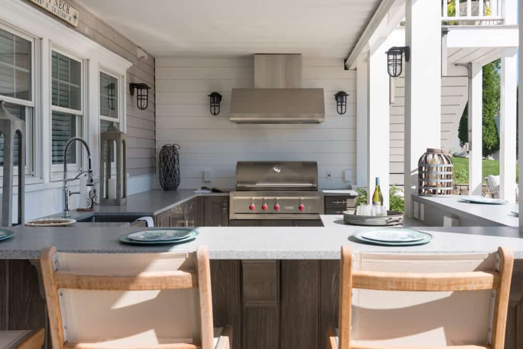 Outdoor kitchen featuring a Wolf appliance stainless steel grill, countertop seating for two, and modern fixtures under a covered patio.
