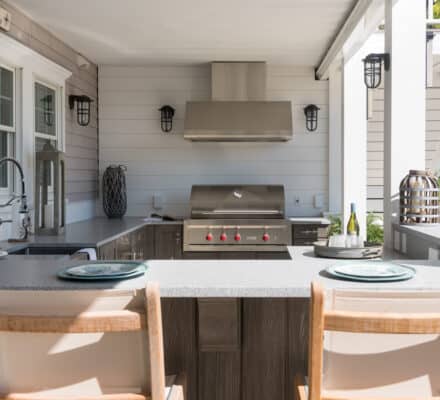 Outdoor kitchen featuring a Wolf appliance stainless steel grill, countertop seating for two, and modern fixtures under a covered patio.