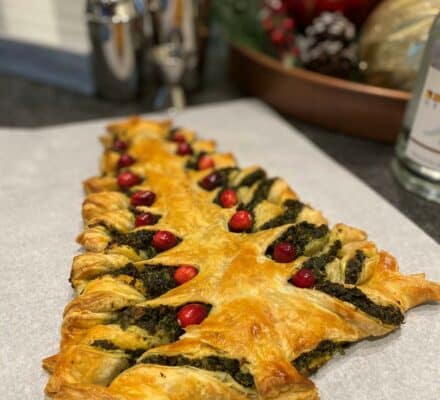 A puff pastry shaped like a Christmas tree, filled with green pesto and decorated with red cranberries, sits on parchment paper—perfect inspiration for your next visit to a kitchen showroom.