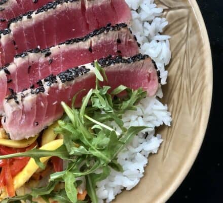A bowl of white rice topped with sesame-crusted seared ahi tuna slices, mixed vegetables, and fresh arugula—perfect inspiration for any appliance showroom or luxury kitchen appliance display.