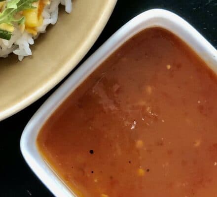 A square white bowl filled with reddish-brown sauce sits next to a tan plate with rice, greens, and vegetables—perfect inspiration for your kitchen showroom or when dreaming up meals using a Wolf appliance.