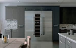 Modern kitchen with dark cabinetry, a large stainless steel refrigerator—showcasing what are sub-zero appliances—with double doors and center wine storage, plus a dining table with candles in the foreground.