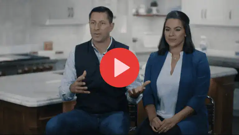 Two people sit side by side in a modern Clarke kitchen, with a play button icon centered over the image, indicating a video.