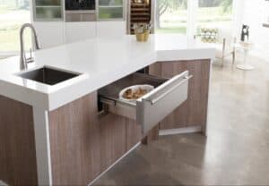 A plate of cookies sits inside a Wolf Appliances warming drawer, built into a modern kitchen island with a sink on a polished concrete floor—a smart invest for any home chef.