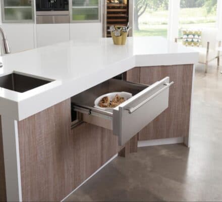 A plate of cookies sits inside a Wolf Appliances warming drawer, built into a modern kitchen island with a sink on a polished concrete floor—a smart invest for any home chef.