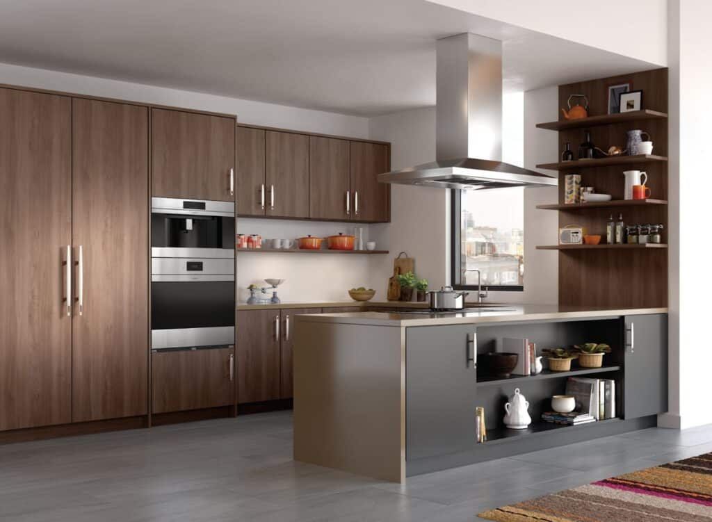 Modern kitchen with wood cabinets, stainless steel oven, open shelving, and a central island featuring a Wolf cooktop and grey cabinetry. Various kitchenware and utensils are visible.