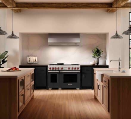 Modern kitchen with large gas range, highlighting the gas vs induction debate, two islands, pendant lights, wood floors, black cabinets, and large windows letting in natural light.