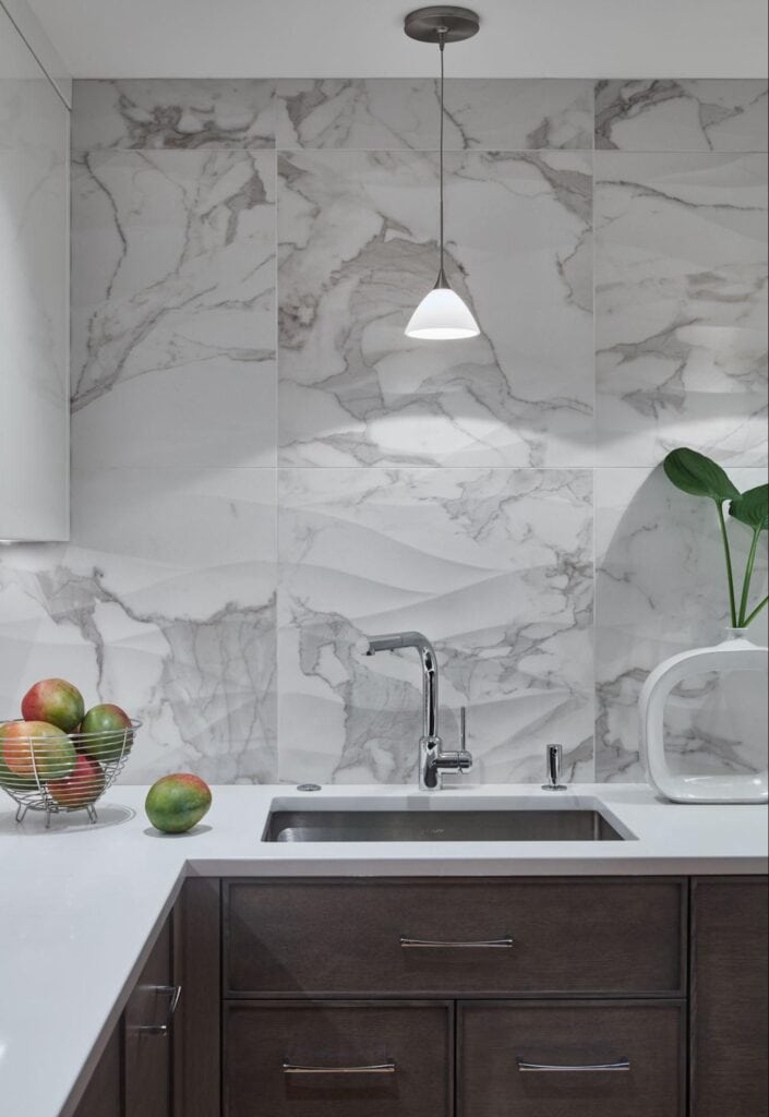 Modern galley kitchen design with a marble backsplash, pendant light, stainless steel sink, dark cabinets, a bowl of apples and mangoes, and a leafy plant—ideal for making the most of narrow space with smart kitchen tips.