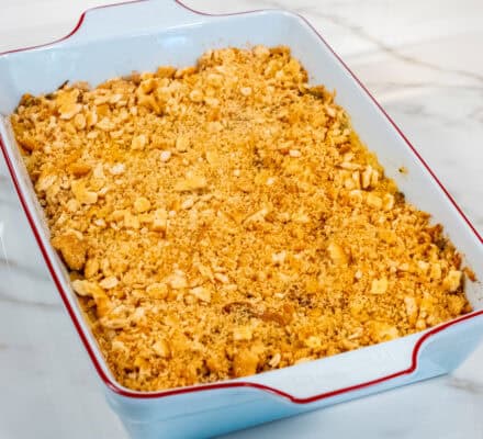 A rectangular baking dish filled with a golden, crumb-topped broccoli cheddar rice casserole sits on a marble countertop.