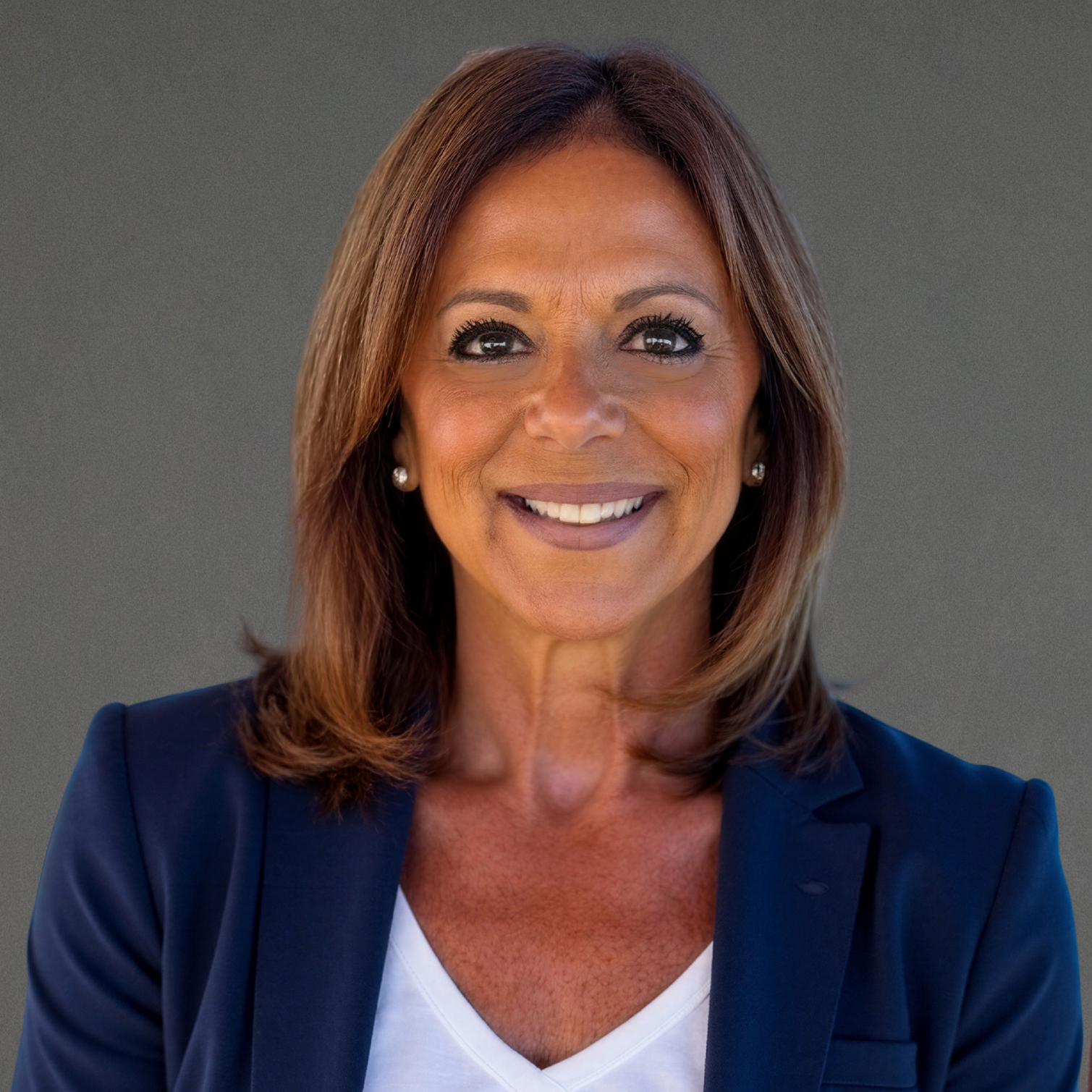 Meet the Clarke Showroom Team: A woman with shoulder-length brown hair, wearing a navy blazer and white top, smiles while posing in front of a plain grey background.